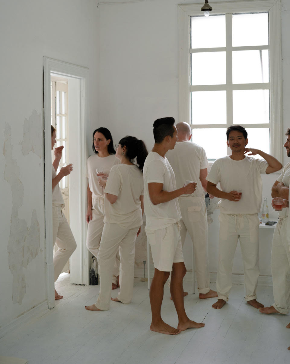 Several people in matching IOAN undyed t-shirts and pants standing in a bright white room with large windows.