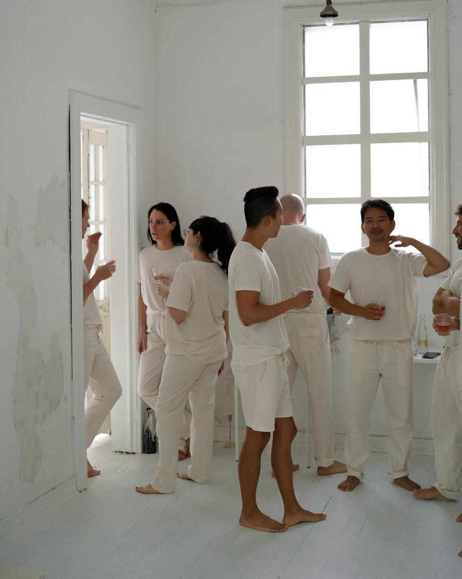 Several people in matching IOAN undyed t-shirts and pants standing in a bright white room with large windows.