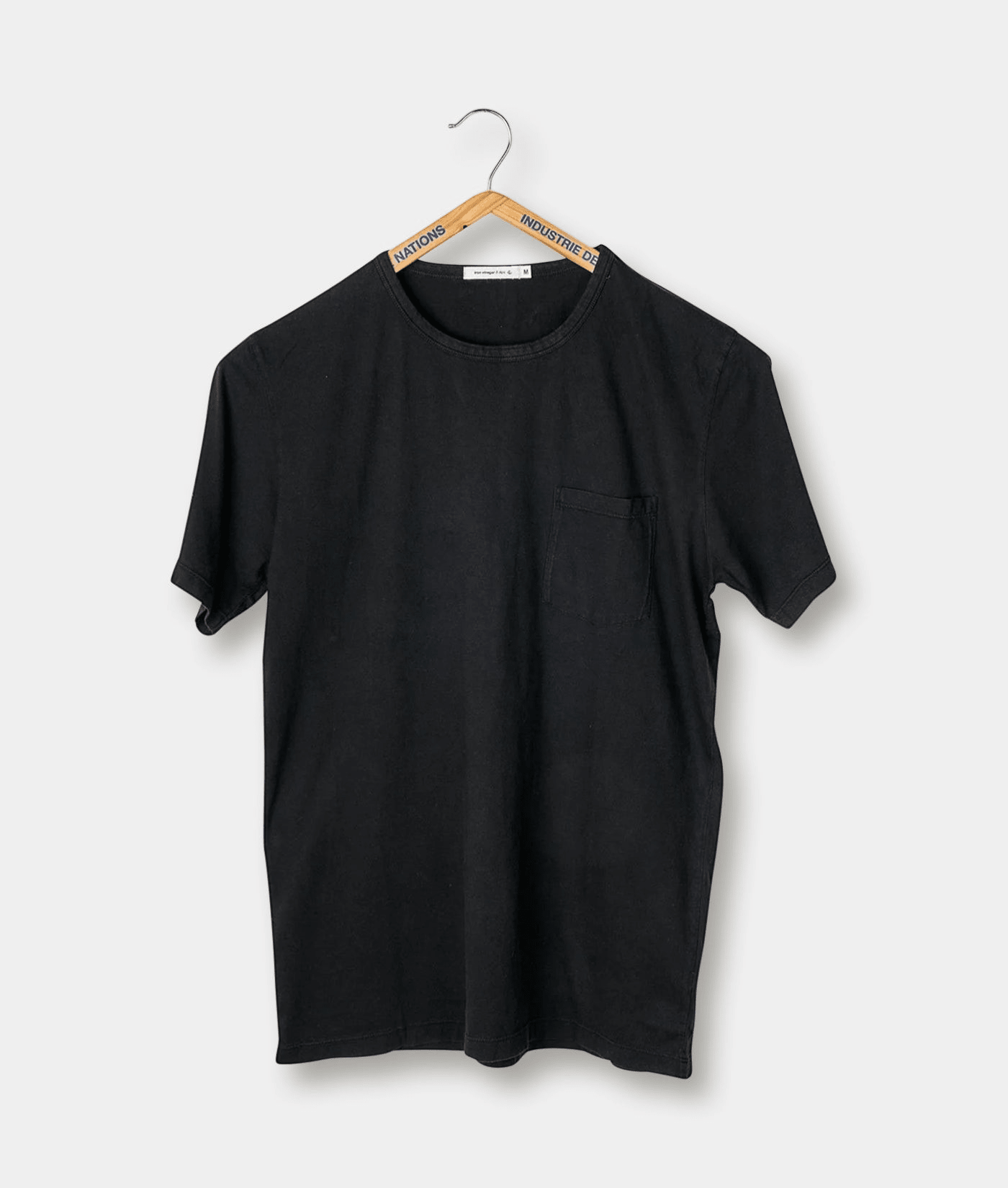 Black t-shirt with front pocket displayed on a hanger - Industry of All Nations