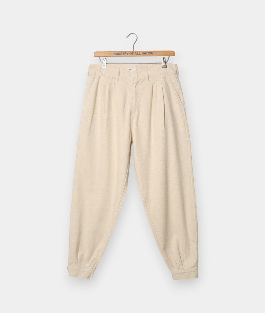 Industry of All Nations cream-colored gaucho pants with a pleated front and tapered leg on a wooden hanger.