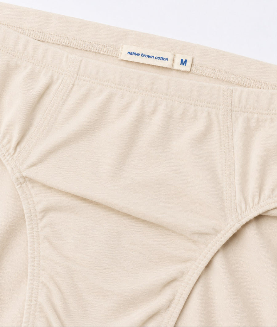 Close-up of a beige underwear brief with a fabric label reading 'native brown cotton' and size 'M' at the waistband.