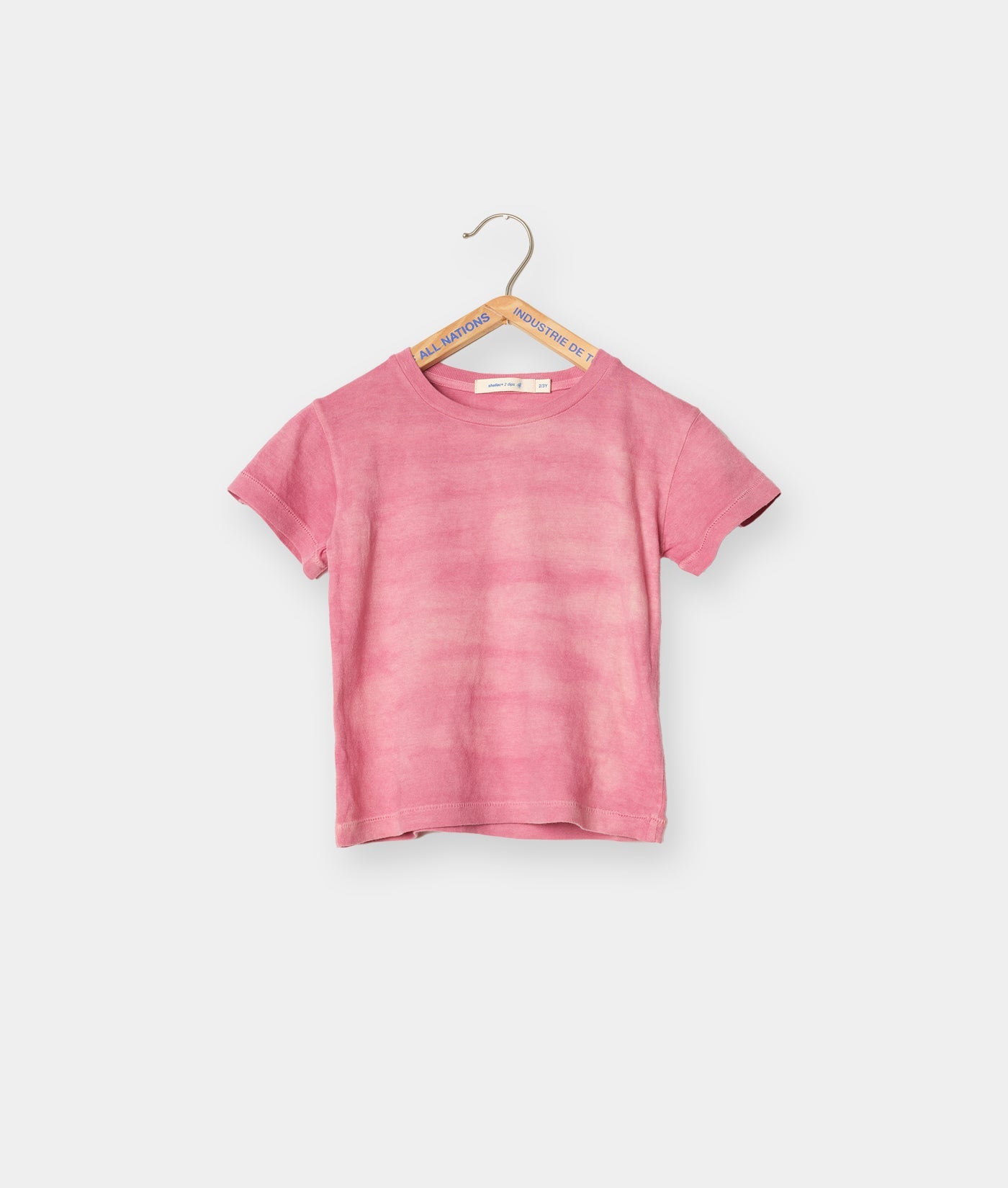 Pink organic cotton t-shirt hanging on wooden hanger with brand tag - Industry of All Nations