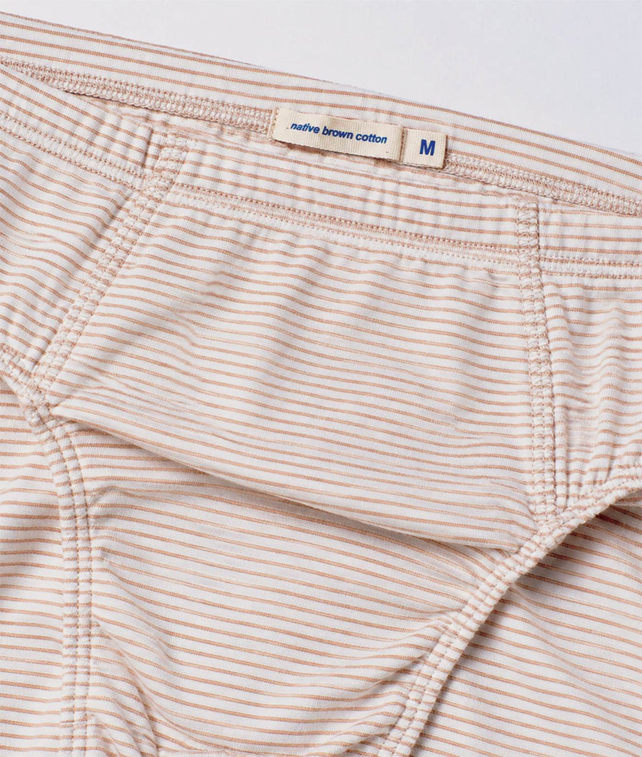 Close-up of a pair of men's underwear with a fine horizontal stripe pattern in beige and white. The waistband features a fabric label that reads 'native brown cotton' and size 'M'.