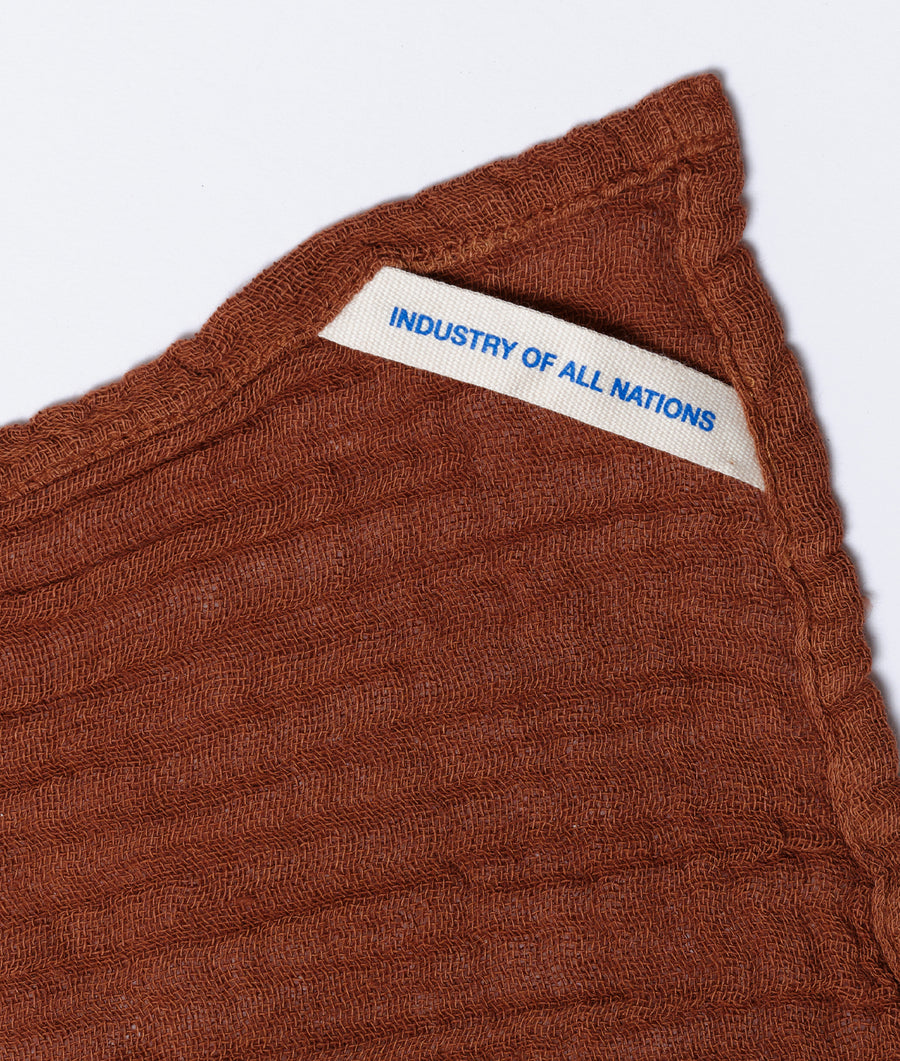 A close-up detail shot of a brown, textured knit garment with a tag that says "Industry of All Nations" - Industry of All Nations