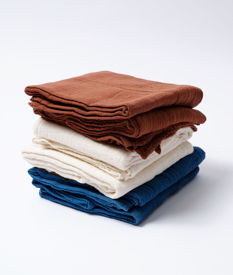 A stack of folded cotton clothing in shades of rust, cream, and navy blue - Industry of All Nations