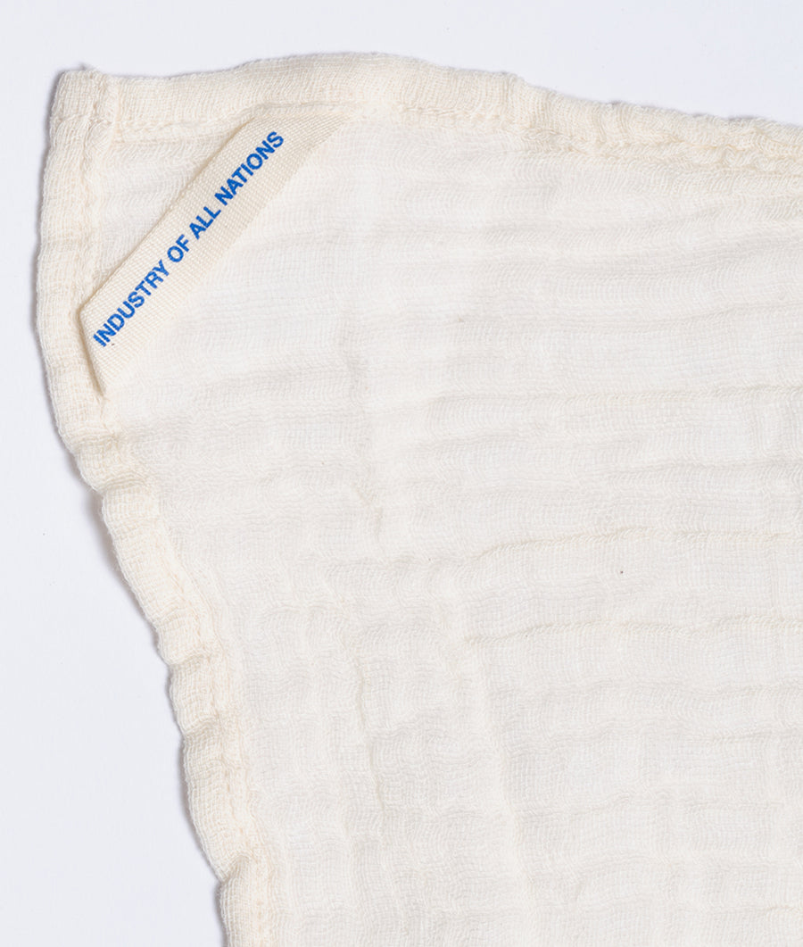 Flat lay image of a white organic cotton towel with "Industry of All Nations" printed in blue text - Industry of All Nations