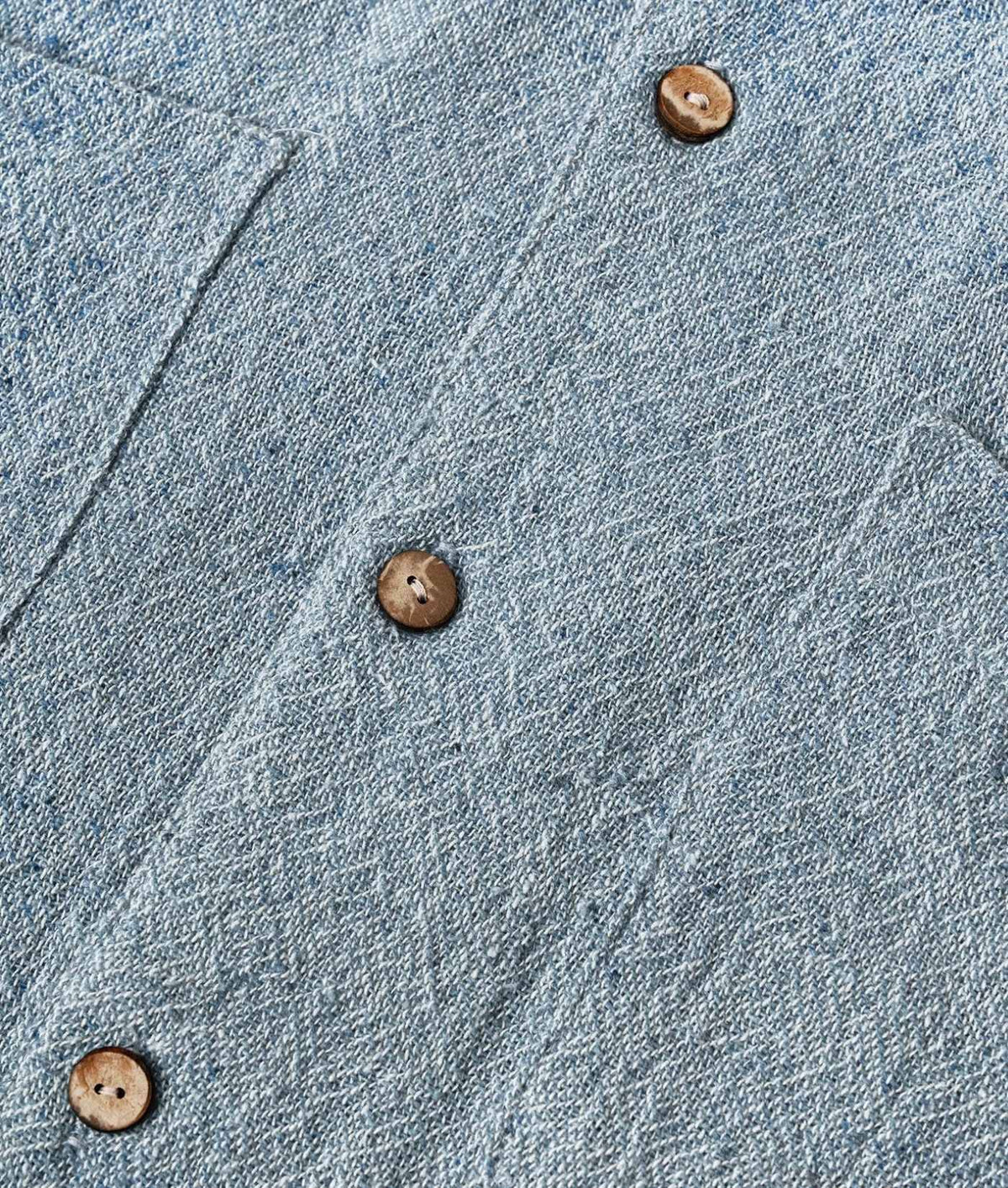 Close-up of a light blue textured fabric, likely linen or a linen-blend shirt material, with three brown buttons arranged diagonally.