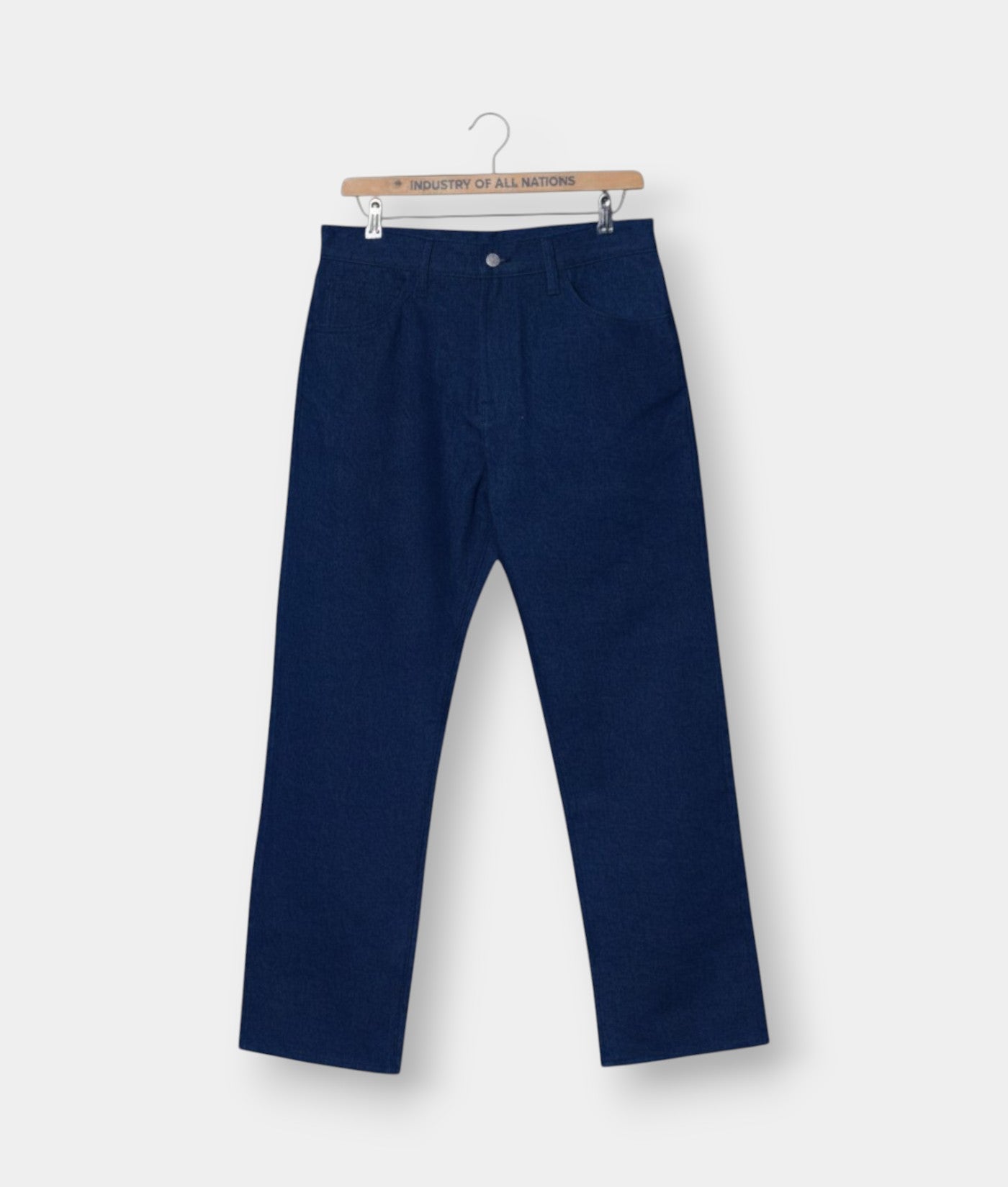 Navy blue cotton pants hanging on a wooden hanger with the brand's "Industry of All Nations" logo - Industry of All Nations