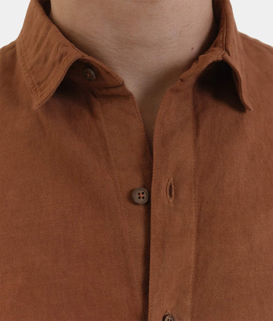 Close-up of a brown linen button-down shirt worn by a model, showing the collar, fabric texture, and buttons.