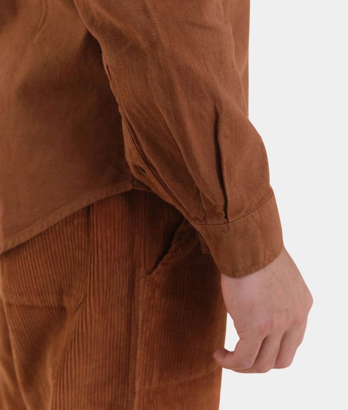 Close-up of a person wearing a brown corduroy long-sleeve shirt and matching brown corduroy pants against a plain light background.