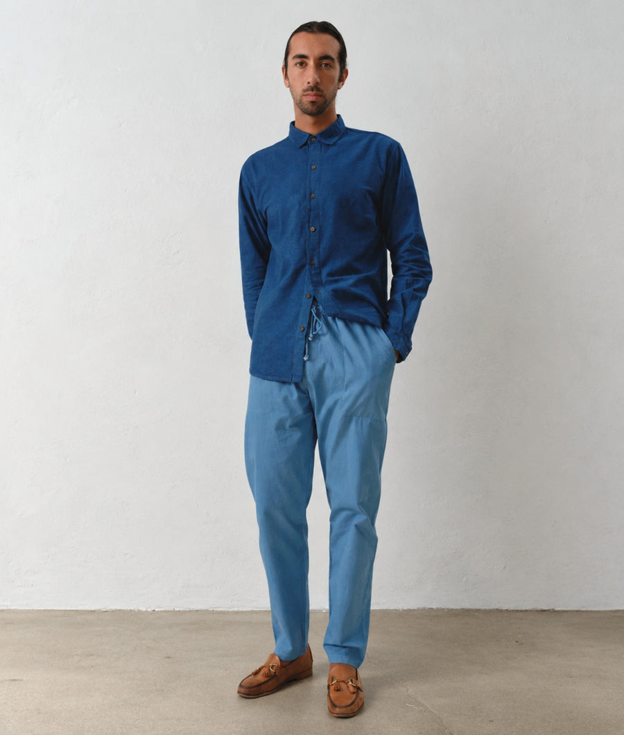 A man modeling the IOAN Pondi Shirt in Indigo 12, paired with IOAN Drawstring Pants, against a plain light gray background.