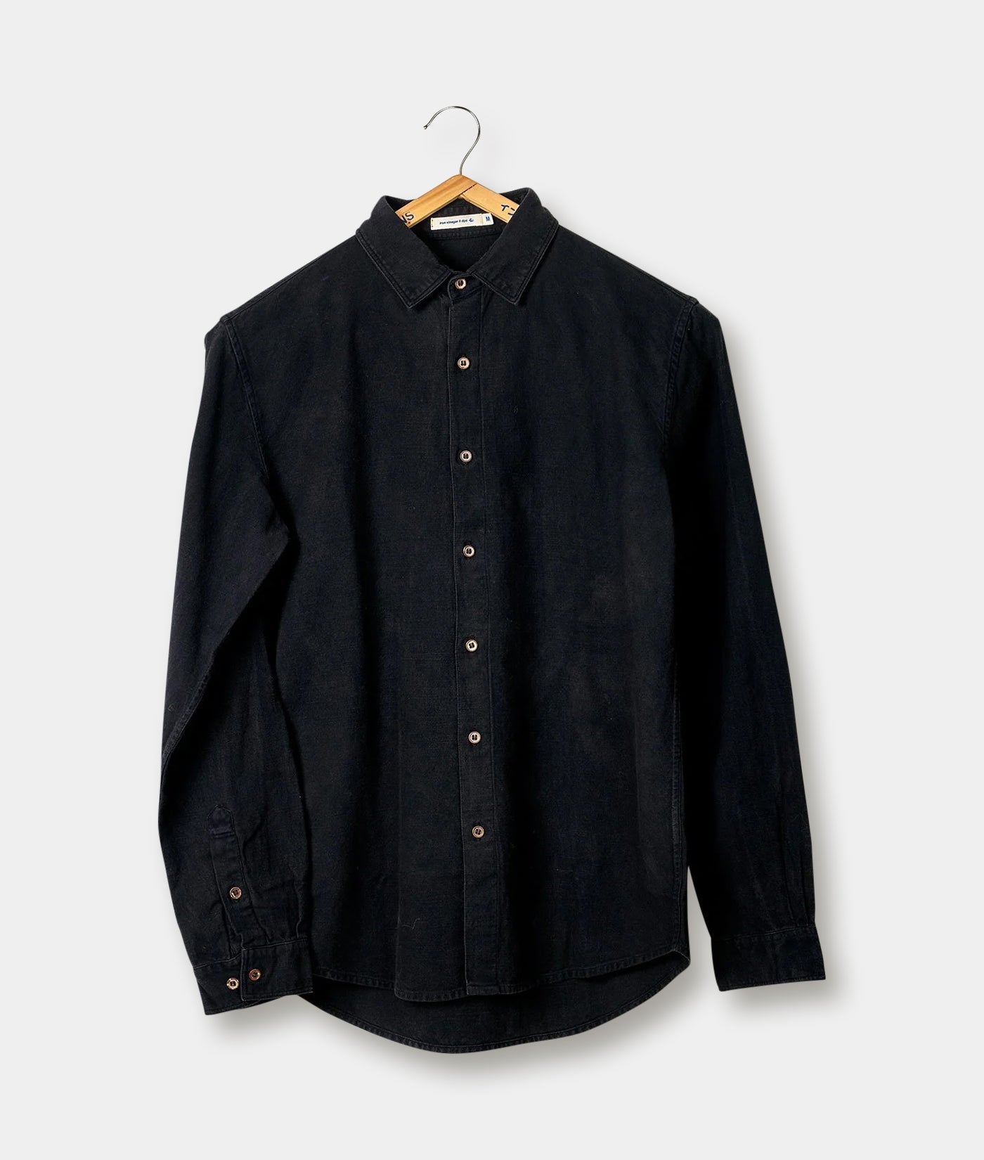 Black denim long-sleeve shirt hanging on a wooden hanger against a plain background - Industry of All Nations
