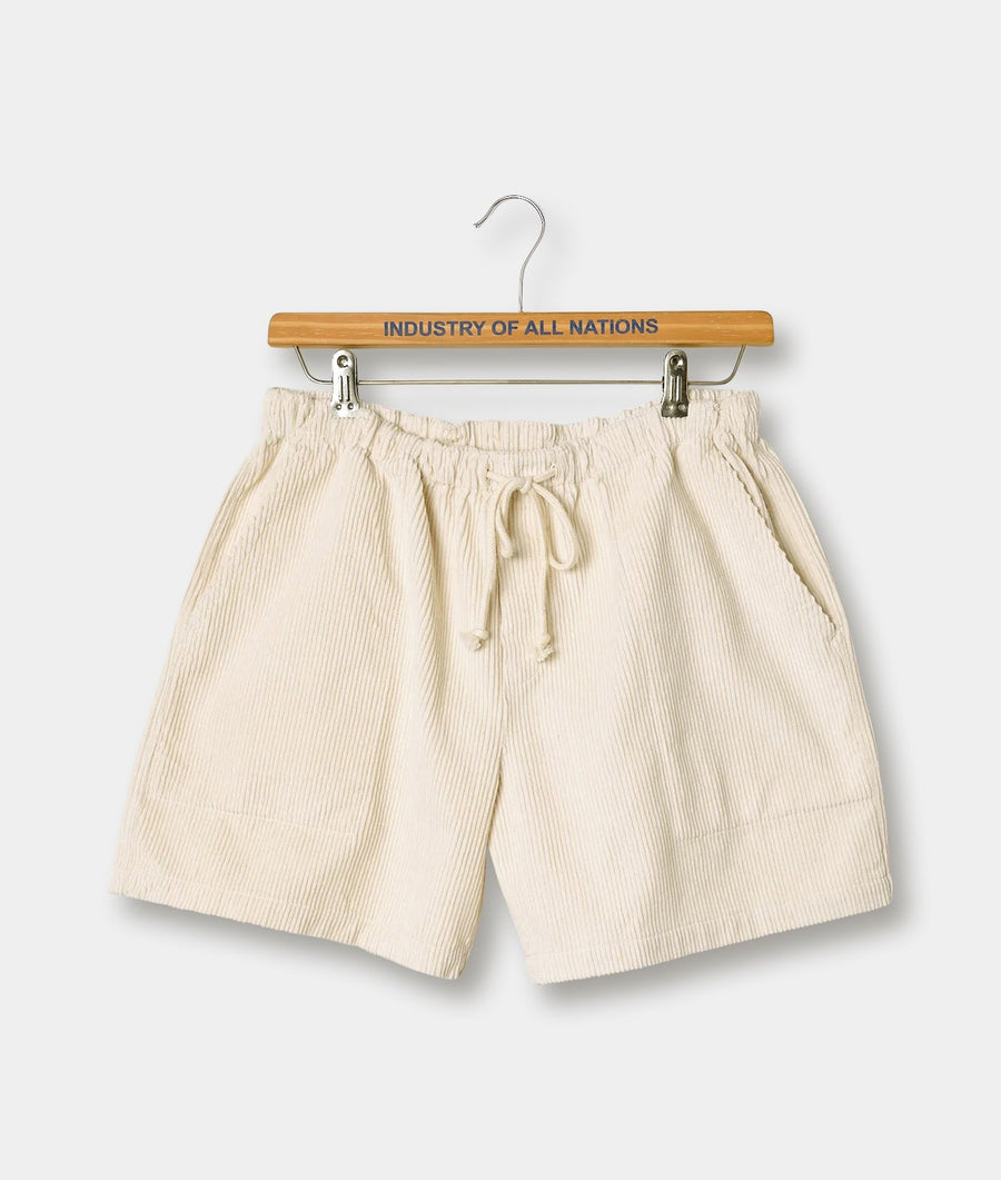 Cream-colored cotton shorts with drawstring waistband, displayed on a wooden hanger with the brand name "Industry of All Nations" printed on it.