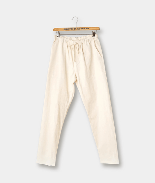 Cream-colored relaxed-fit organic cotton pants with drawstring waist, displayed on a wooden hanger - Industry of All Nations