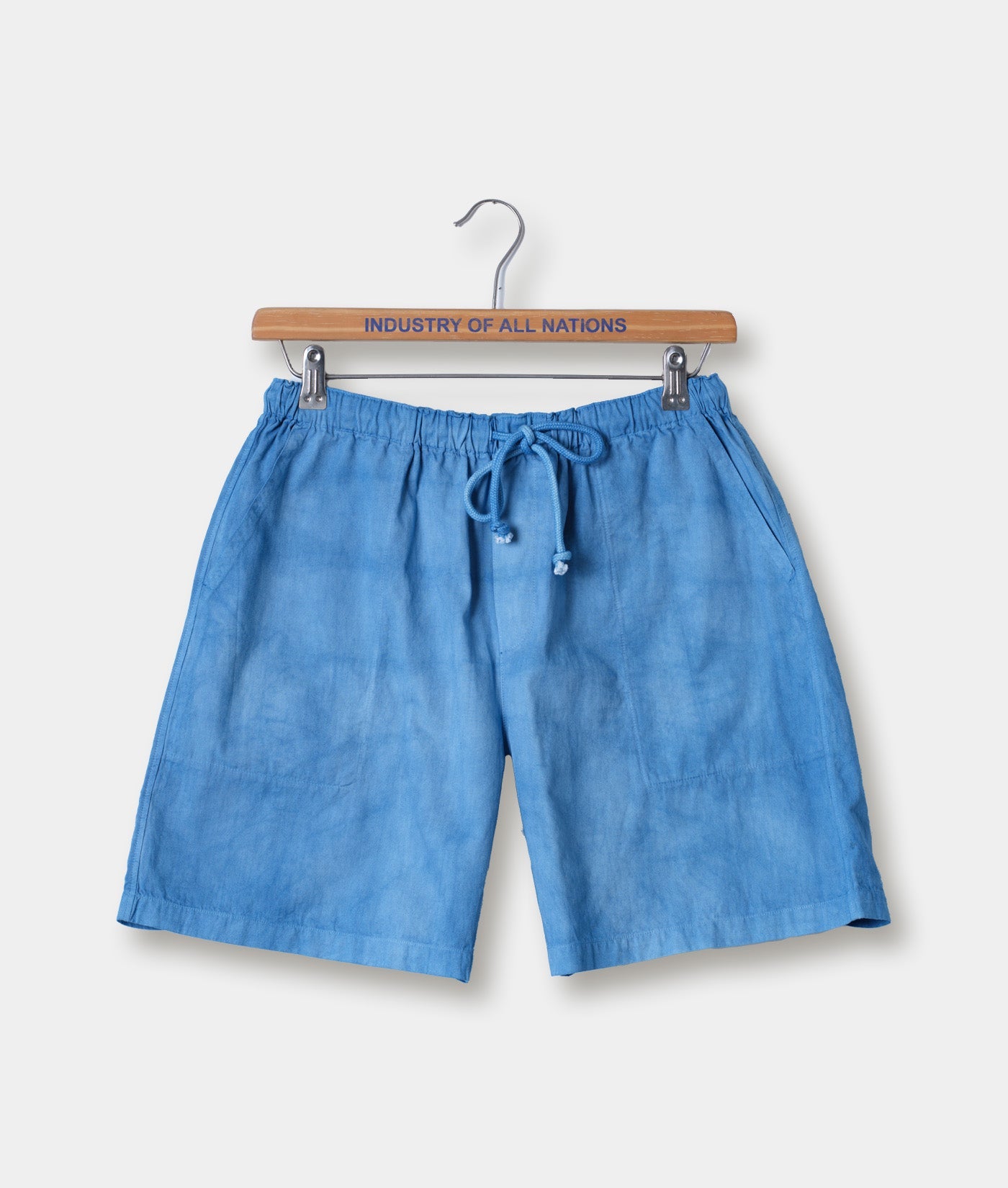 Blue linen drawstring shorts hanging on a wooden hanger with the brand name "Industry of All Nations" printed on it - Industry of All Nations