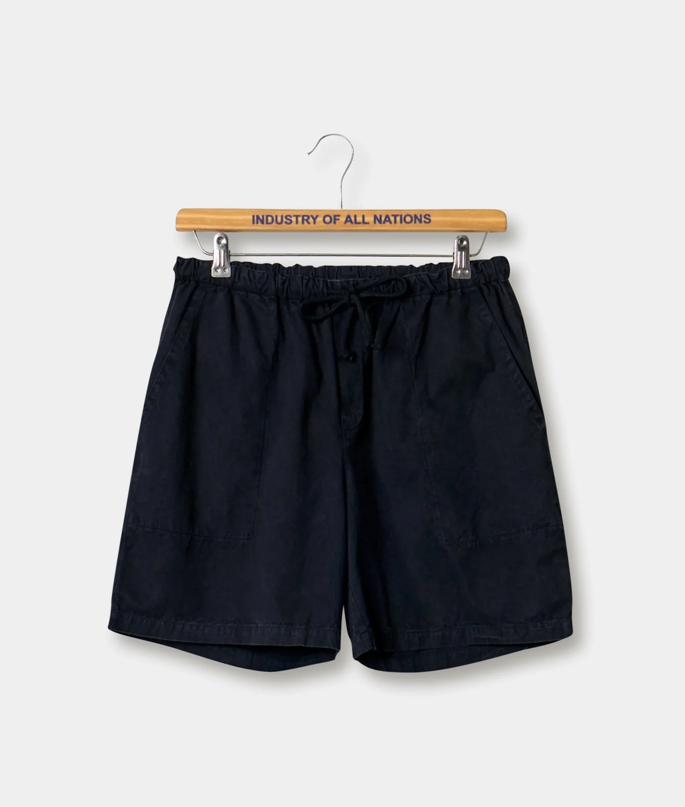 Black drawstring shorts hanging on a wooden hanger with "INDUSTRY OF ALL NATIONS" printed on it - Industry of All Nations