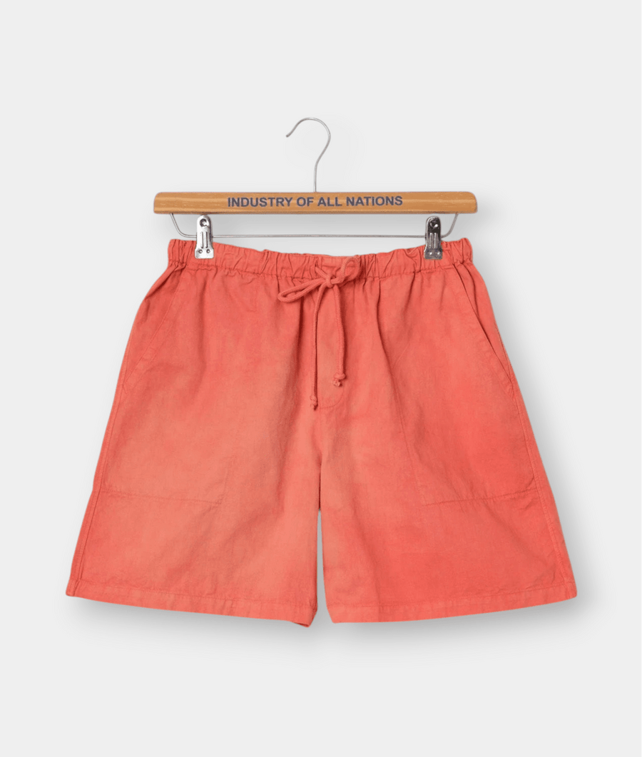 Orange linen shorts with drawstring waist displayed on a wooden hanger with "Industry of All Nations" text - Industry of All Nations
