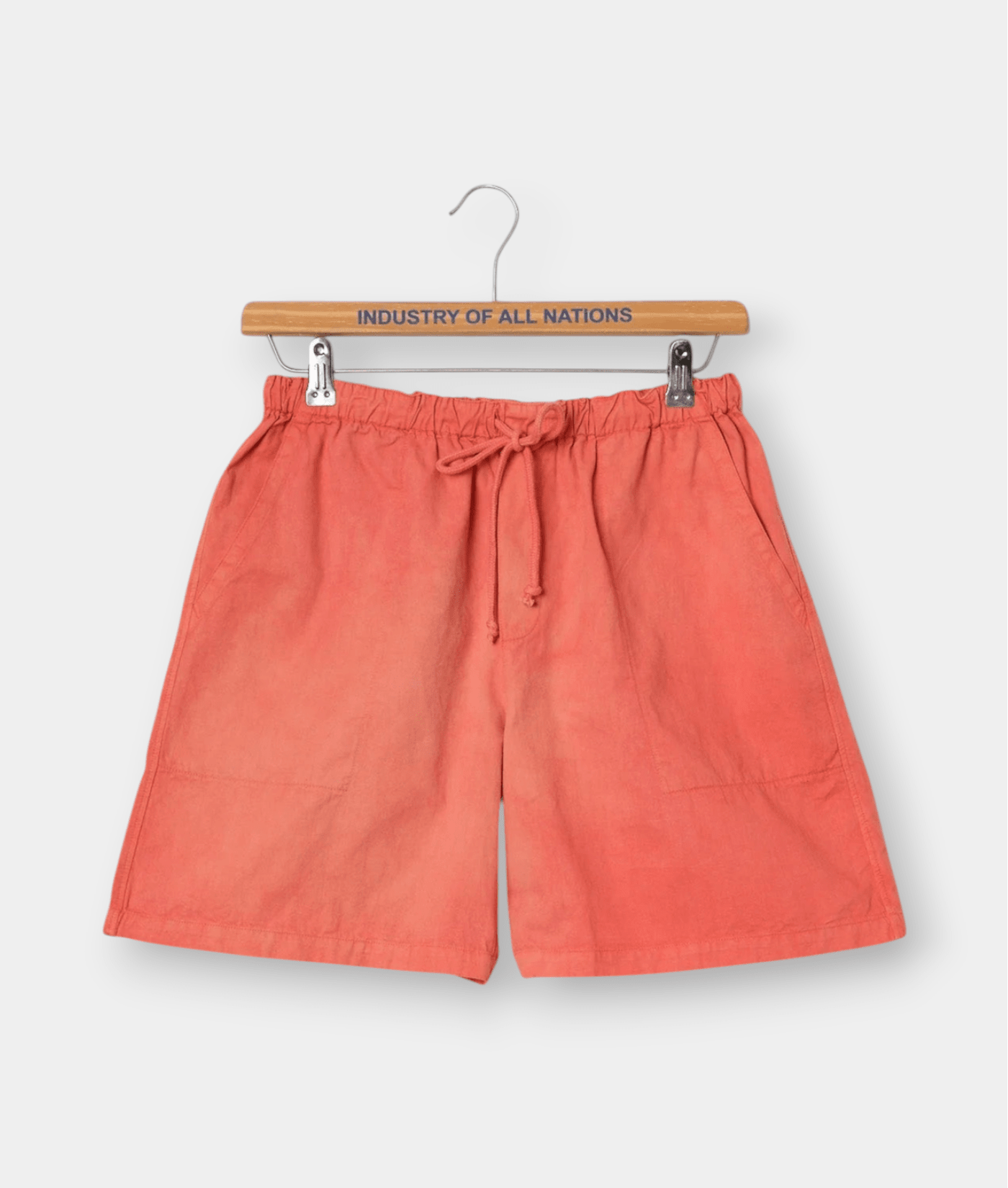 Orange linen shorts with drawstring waist displayed on a wooden hanger with "Industry of All Nations" text - Industry of All Nations