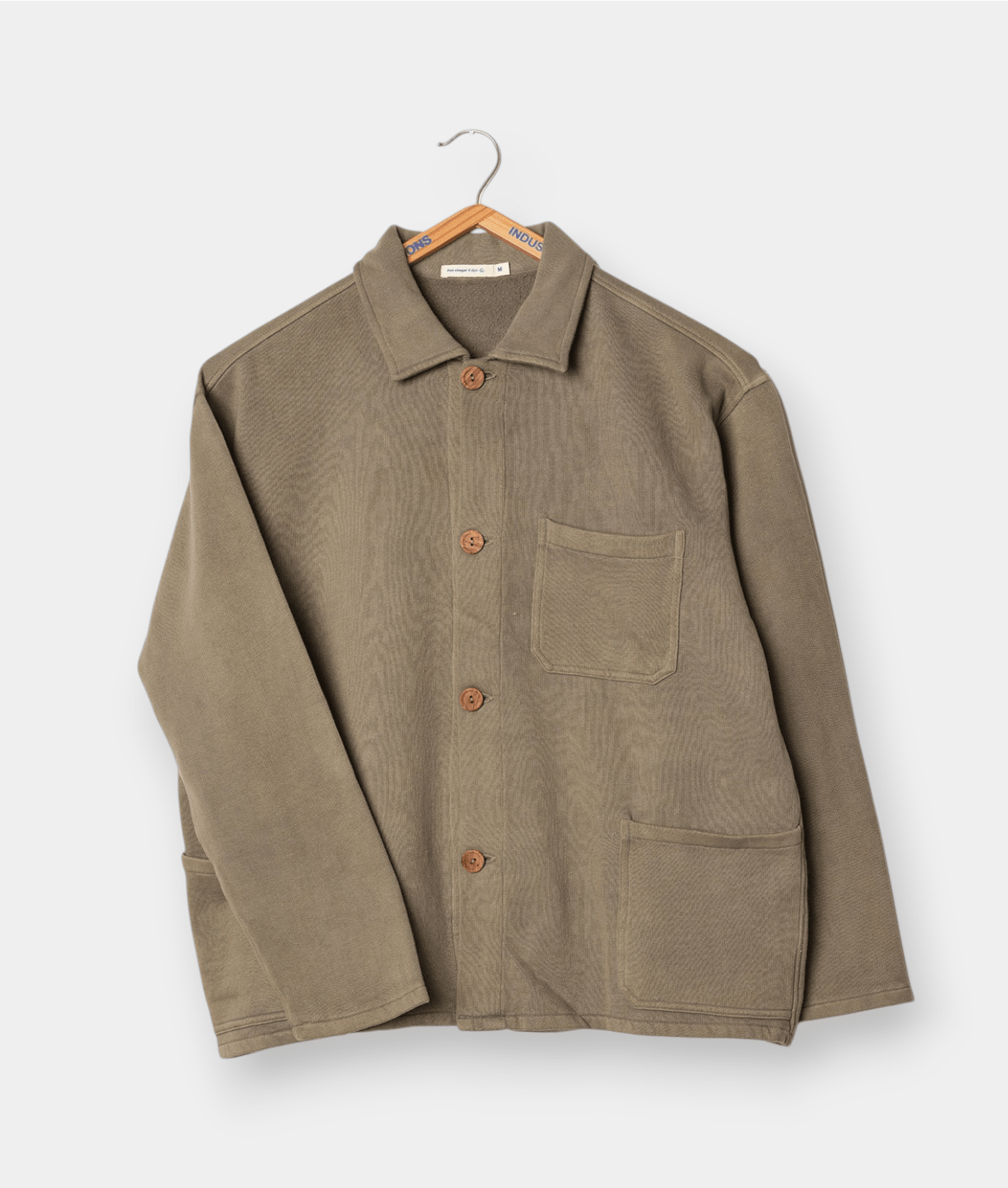 Tan-colored cotton workwear jacket displayed on a clothes hanger - Industry of All Nations