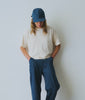 Man wearing an off white t-shirt, blue jeans and blue baseball cap against a white background