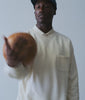 Model in a cream cotton sweatshirt and navy cap tossing a leather ball in studio - Industry of All Nations