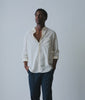 Model in an off-white cotton button-down shirt worn open with navy trousers - Industry of All Nations