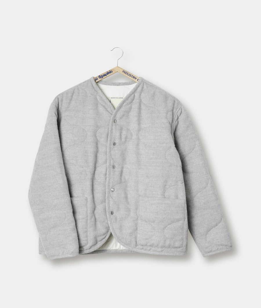A gray collarless quilted jacket hanging on a wooden hanger with an "Industry of All Nations" tag - Industry of All Nations