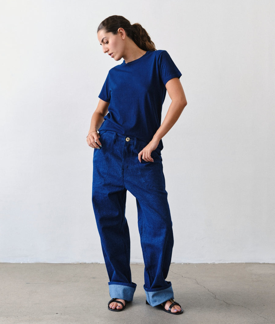 A woman stands in a studio wearing a dark blue short-sleeve t-shirt and matching dark blue wide-leg denim pants with rolled cuffs, paired with black sandals.