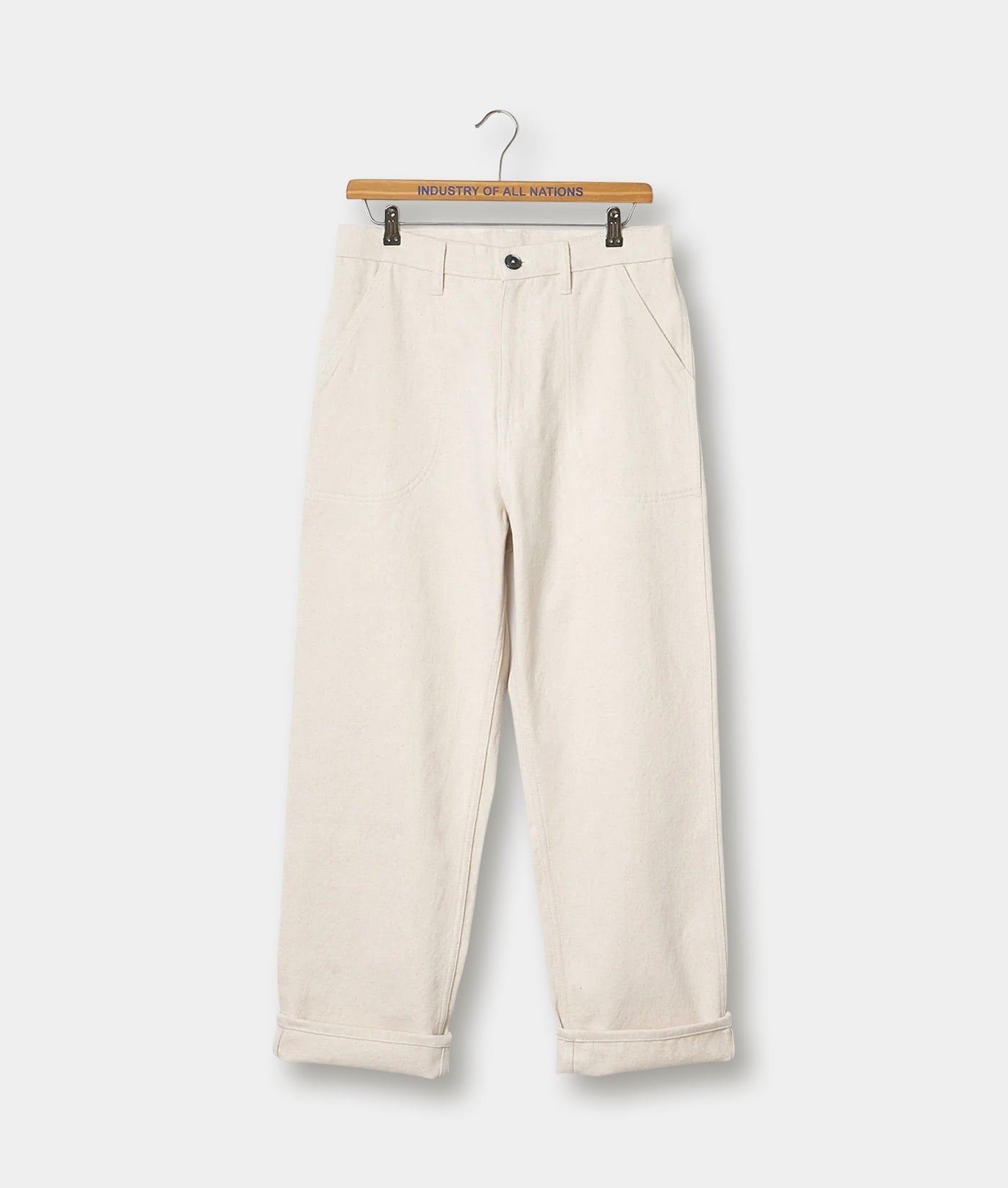 A pair of off-white, loose-fitting, cuffed cotton pants displayed on a wooden hanger with the text "Industry of All Nations" - Industry of All Nations