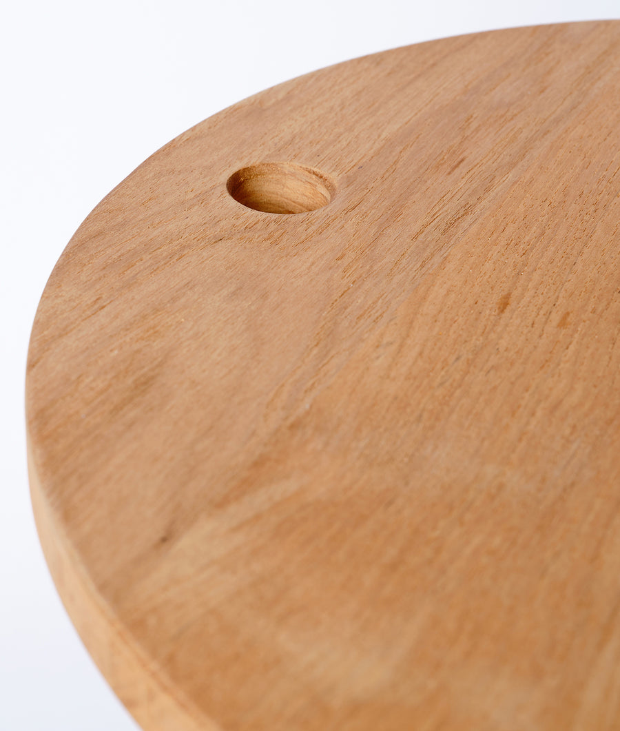 A close-up image of a wooden cutting board or trivet with a simple round hole in the center - Industry of All Nations