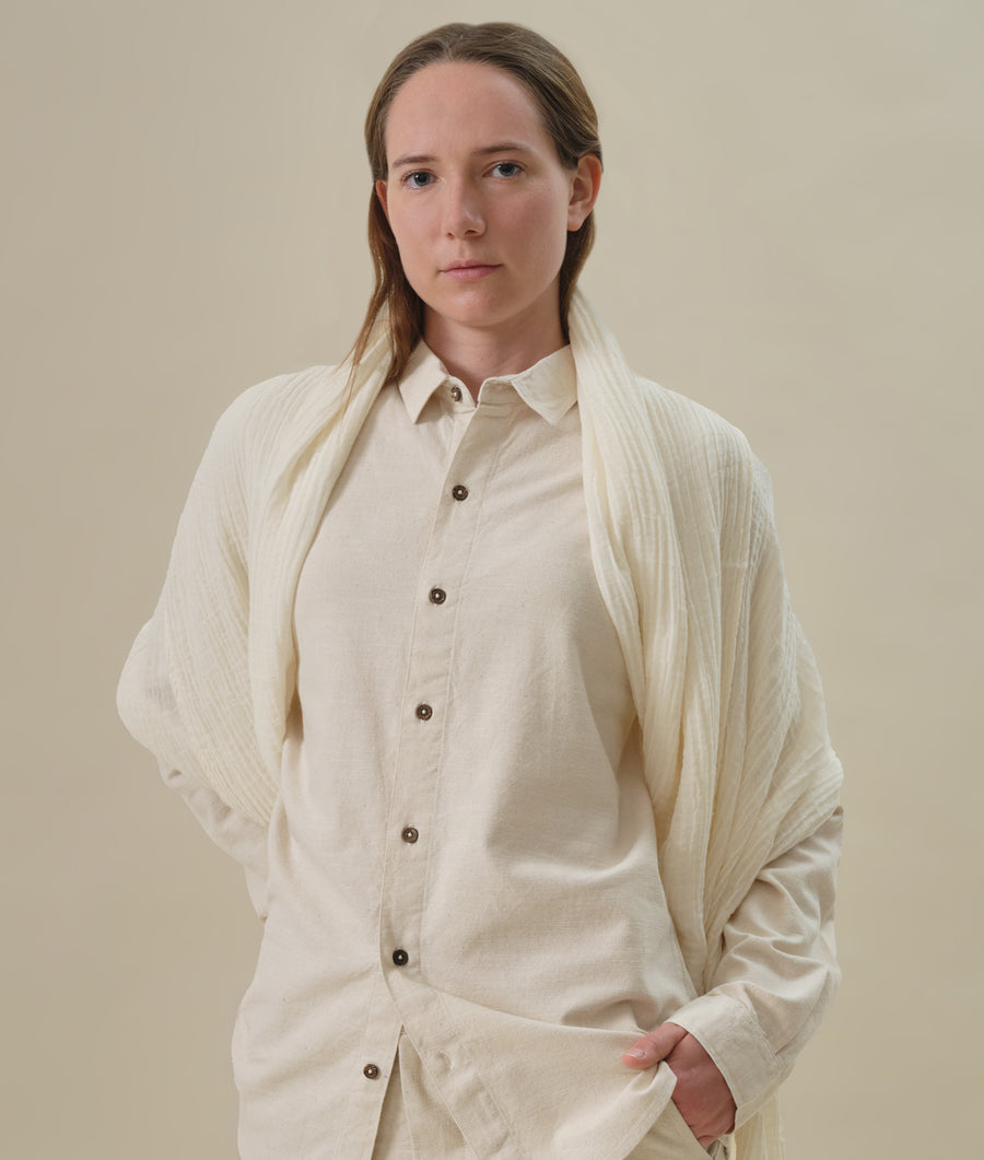 A woman wearing a long-sleeved, cream-colored pleated shirt from Industry of All Nations.