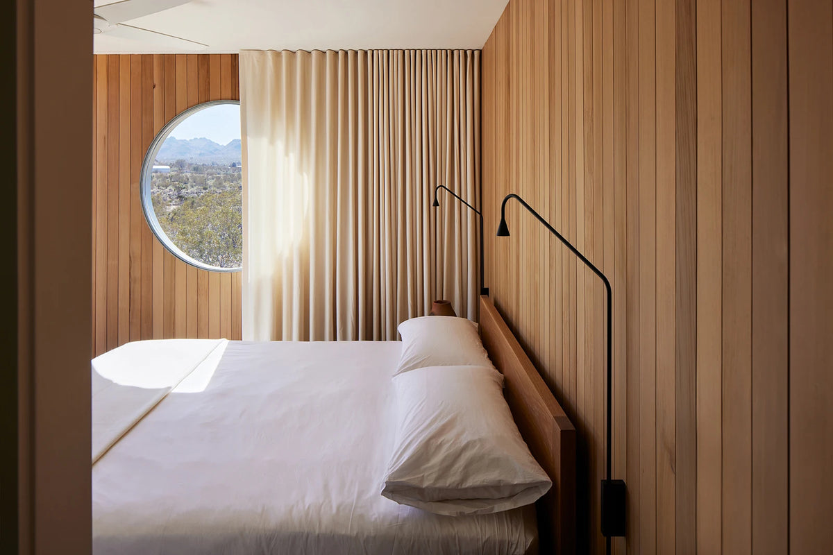 White bedding and cedar walls beside curtains and a round window