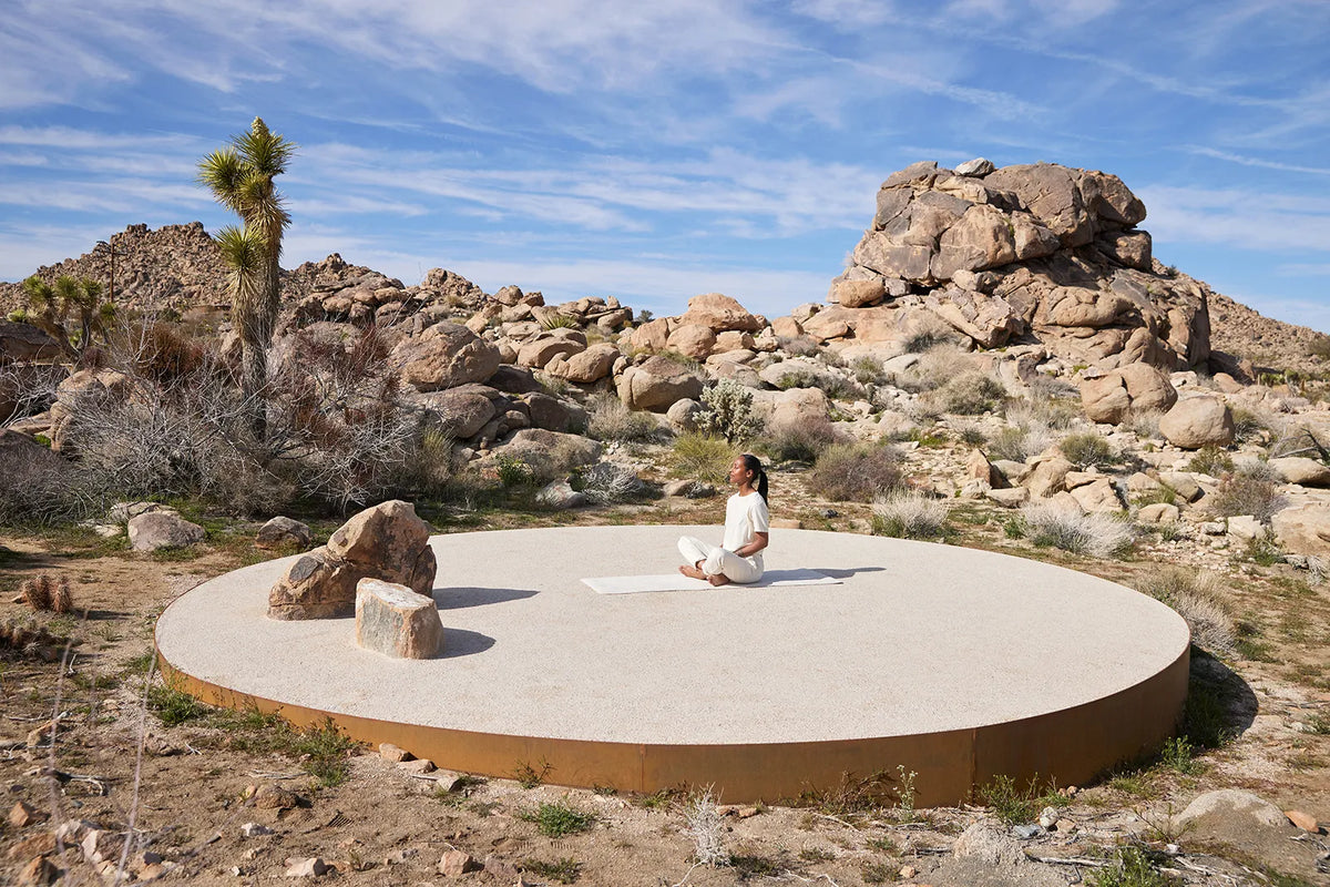 A person meditating on the circular landing pad among Joshua trees and granite boulders