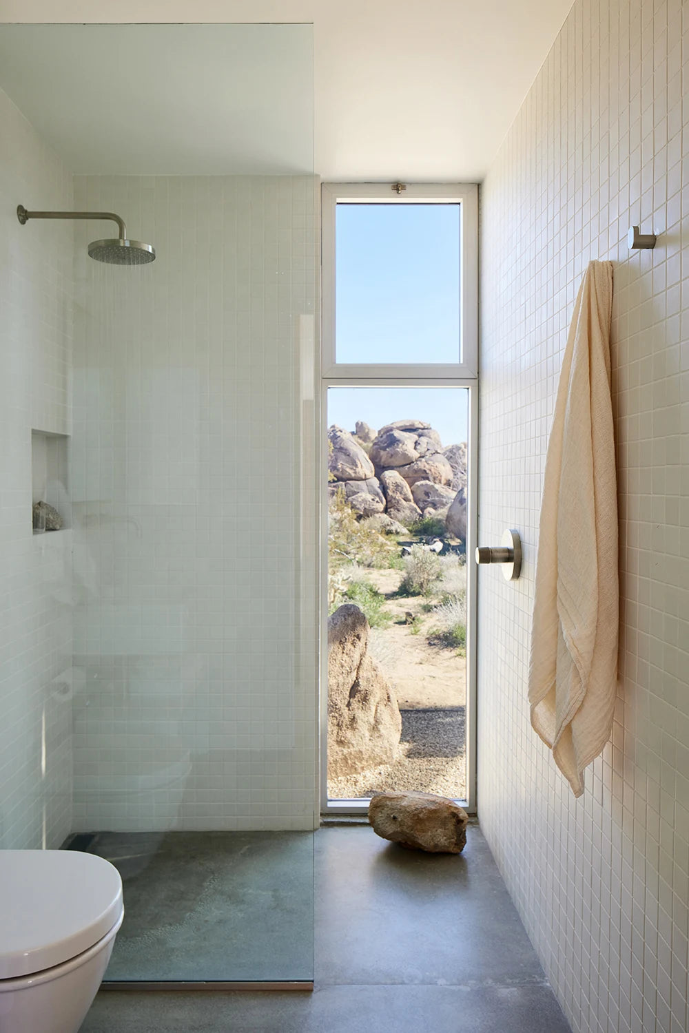 Daylight in the tiled bathroom, with an open glass door framing desert boulders