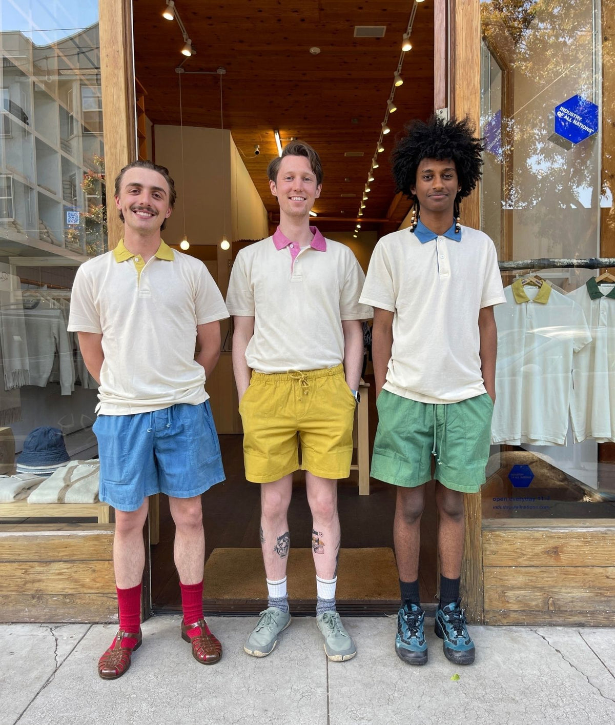 Three men wearing IOAN Sport Polo Shirts with contrasting collars, standing side by side in front of the IOAN store.