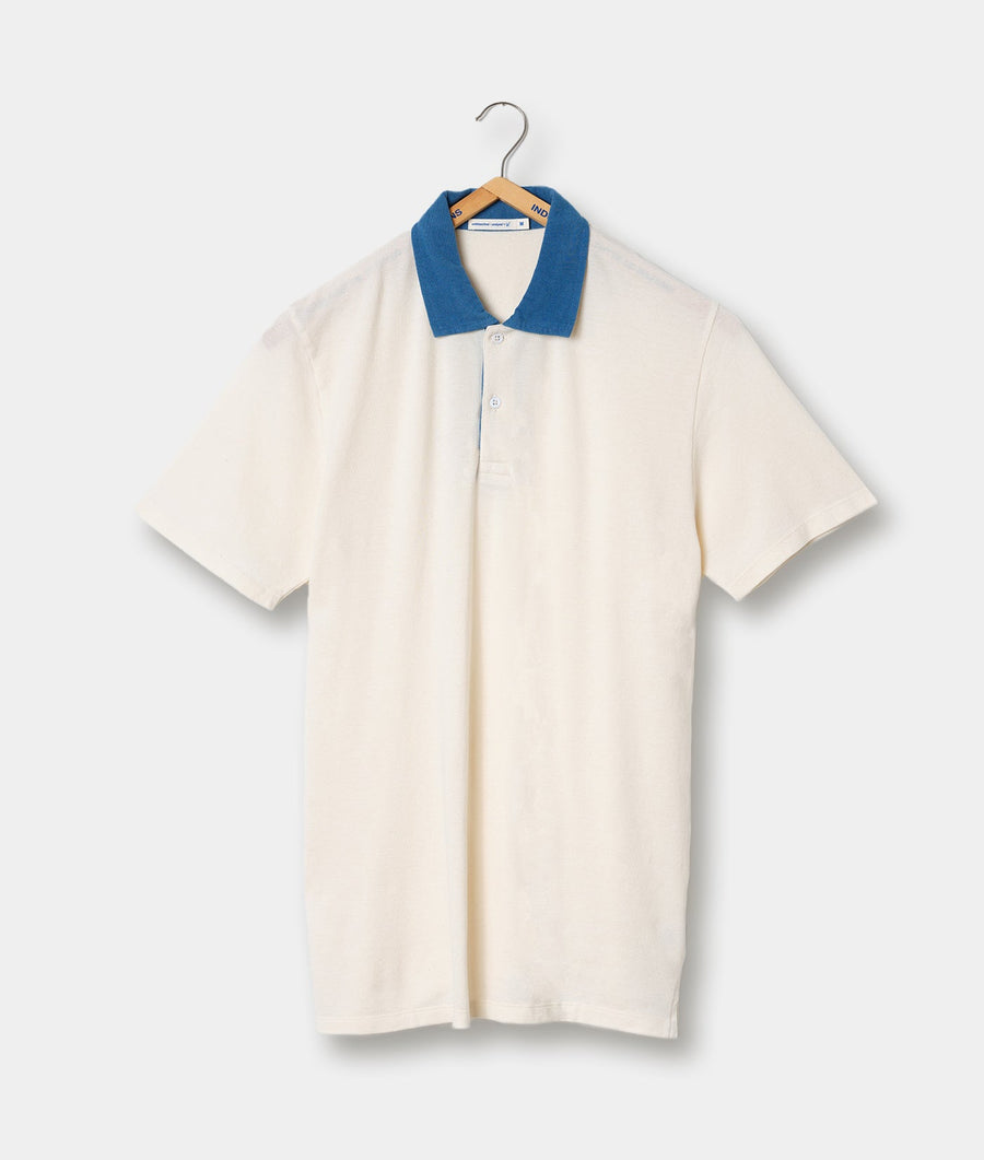 Cream-colored polo shirt with a blue collar and buttons, displayed on a hanger - Industry of All Nations