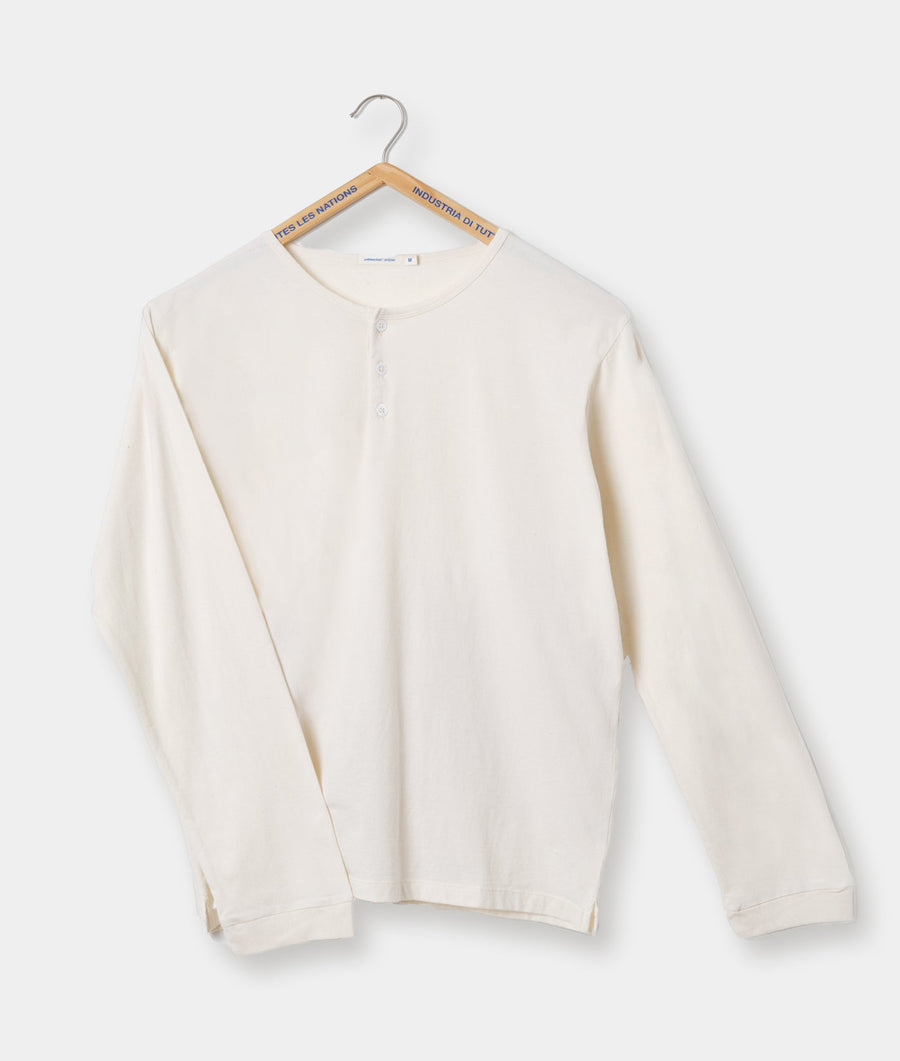 A white, long-sleeved knit shirt hanging on a wooden hanger with "Industria di Tuti" (Industry of All Nations) and "Ites les nations" (United Nations) printed on the hanger - Industry of All Nations