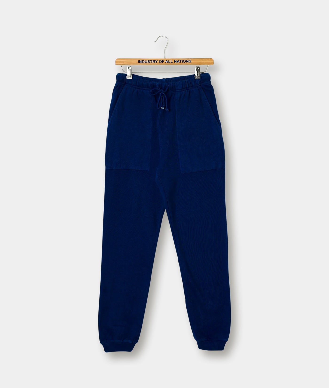 Navy blue sweatpants in a flat lay on a white background, displayed on a wooden hanger with "Industry of All Nations" label. - Industry of All Nations