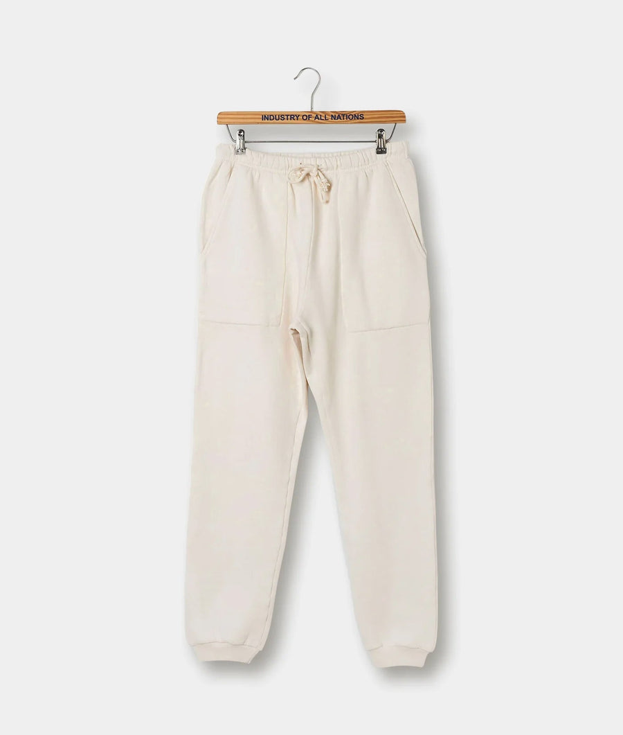 A pair of relaxed-fit, cream-colored cotton sweatpants displayed on a wooden hanger with the brand name "Industry of All Nations" printed on it.