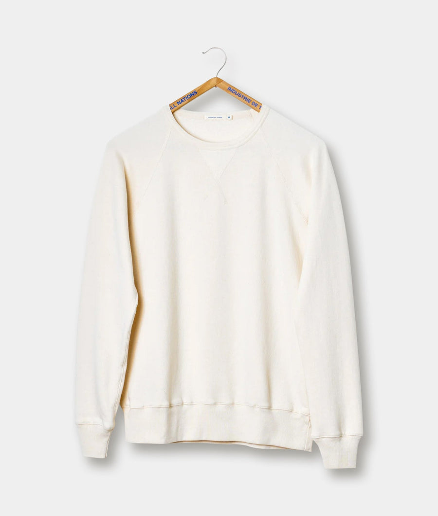A white cotton crewneck sweatshirt hanging on a wooden hanger with an "All Nations Industry de l" tag - Industry of All Nations