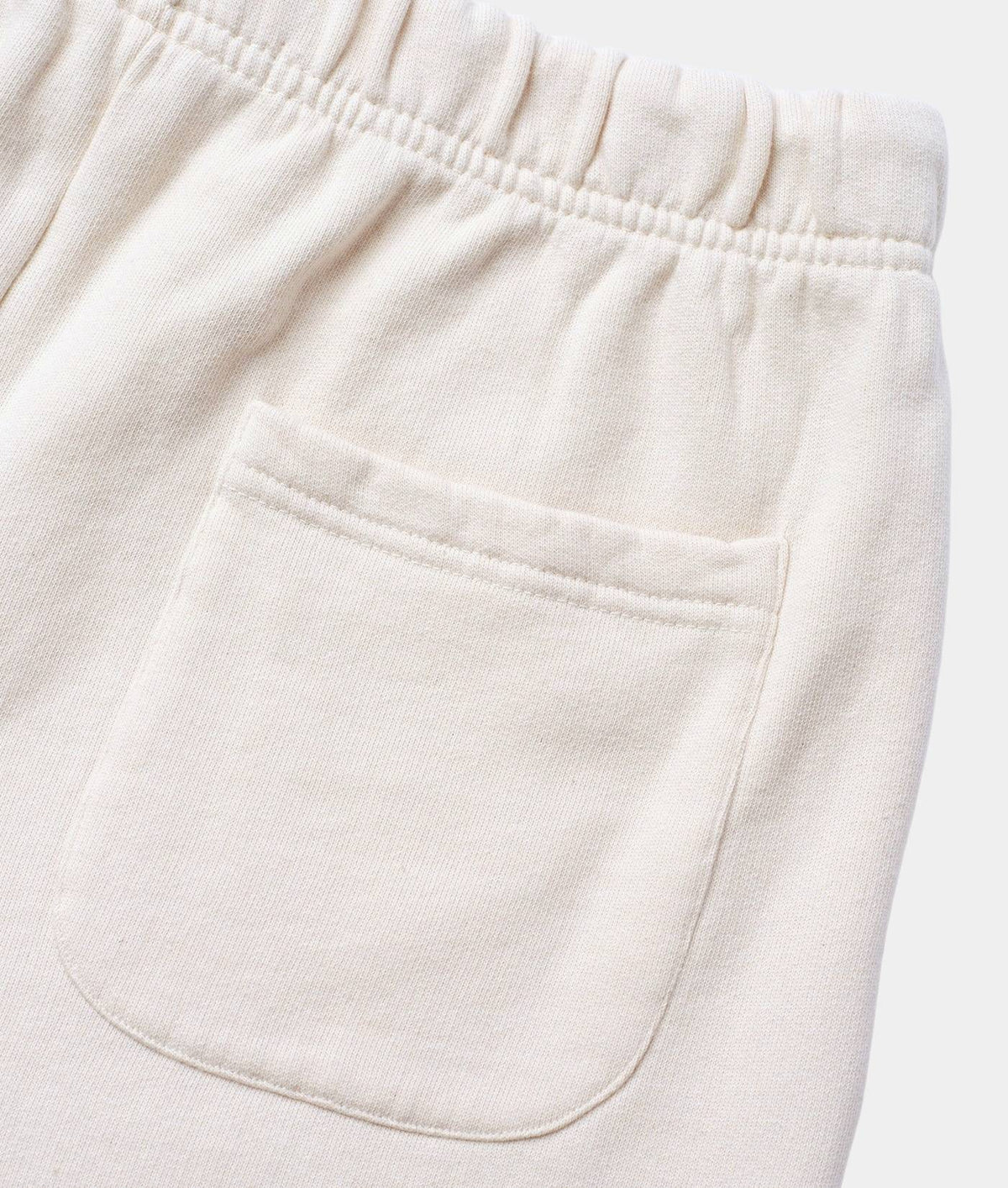 Close-up of off-white or cream-colored fabric pants showing an elastic waistband and a front patch pocket.