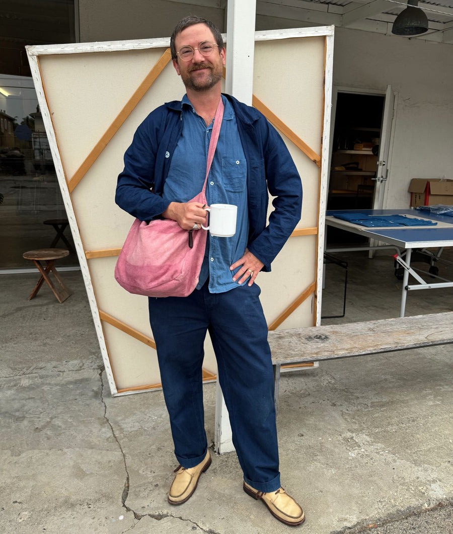 An IOAN team member wearing the Shellac Tote Bag at IOAN HQ, standing in front of a large canvas frame and holding a white mug.
