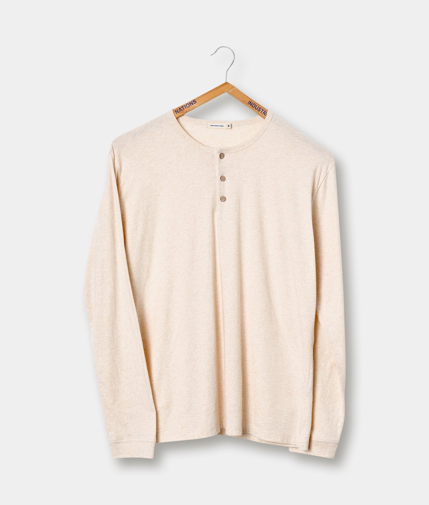 Beige long-sleeved cotton shirt hanging on wooden hanger with "NATIONS INDUSTRY" label - Industry of All Nations