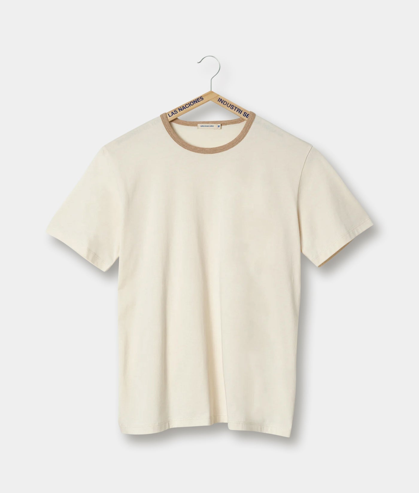 Cream-colored t-shirt with brown trim, displayed on a hanger against a white background - Industry of All Nations