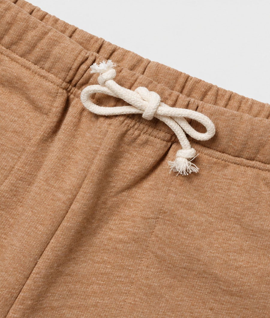 Close-up of tan heathered sweatpants with a white drawstring tied in a knot at the elastic waistband.