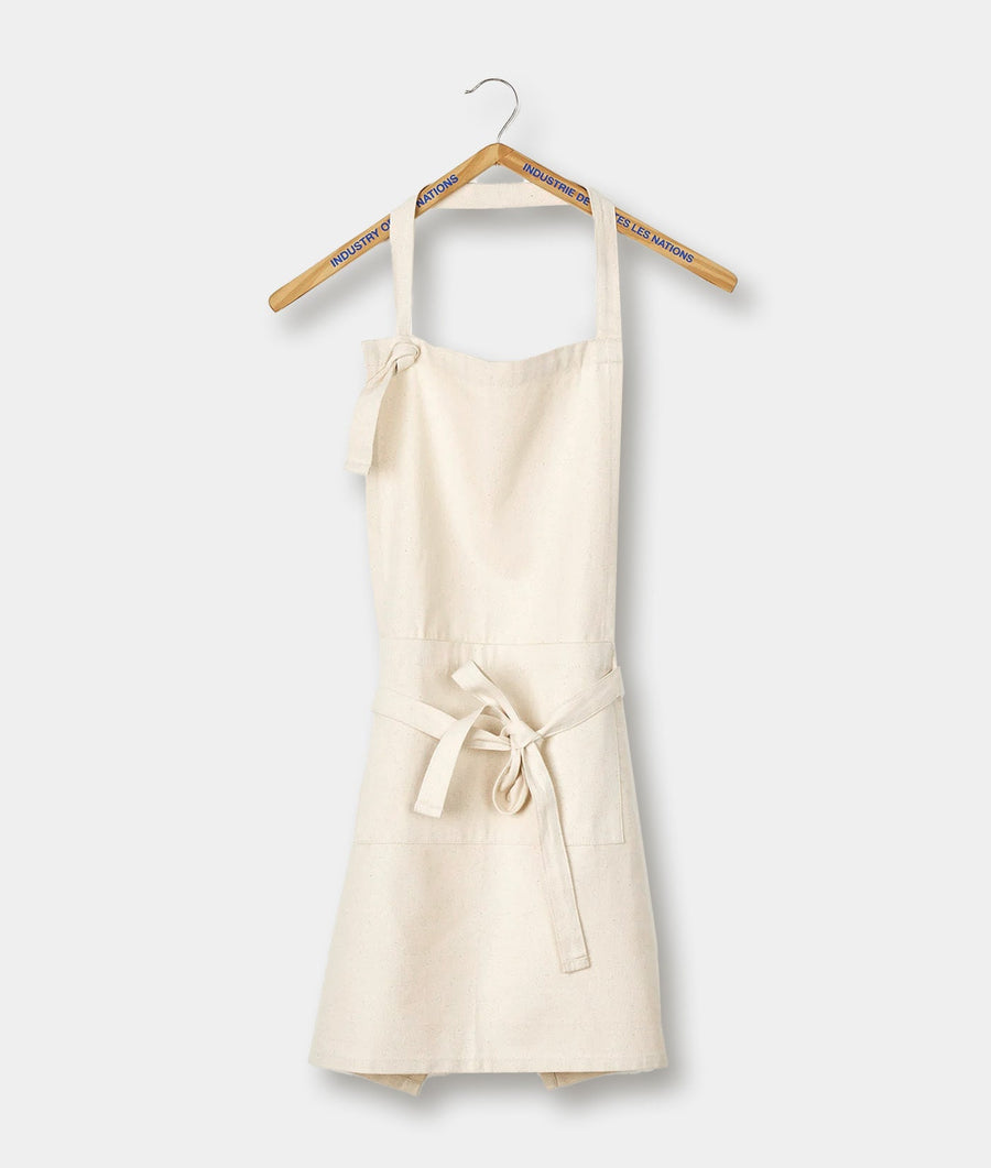 A beige canvas apron with pockets, shown hanging on a wooden hanger with "Industrie des Nations" text - Industry of All Nations
